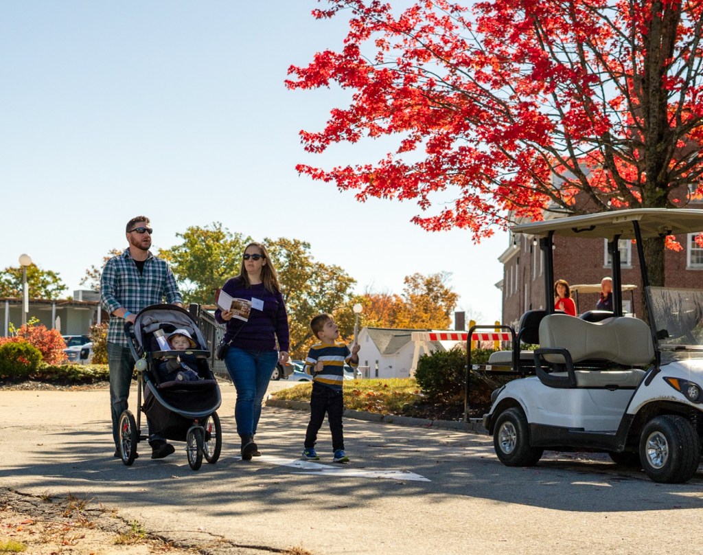 Parents walking with stroller and toddler under red maple leaf foliage.